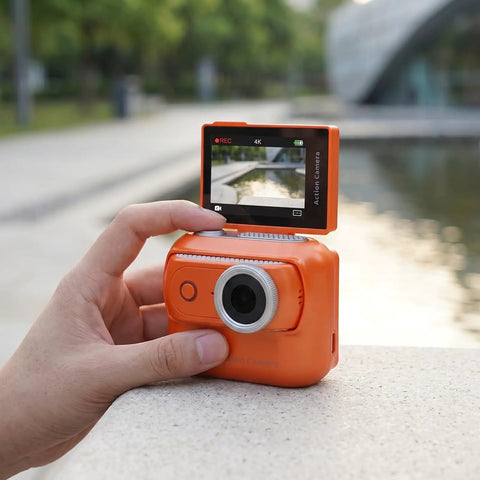 4K Magnetic Action Camera With 48MP Sensor Dual Battery System 2.0 Inch Flip Touch Screen EIS Stabilization 200fps Slow Motion App Control For Vlog And Adventure Easy Magnetic Mount For Helmets And Chest Straps Orange, in hand near water, with screen flipped up.