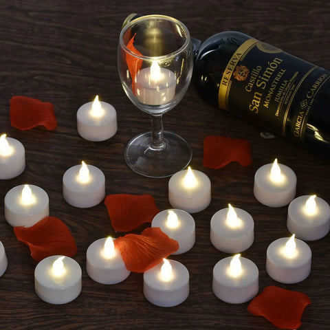 100 Count Battery Powered LED Tea Lights Flameless Flickering Warm White Candles Long Lasting CR2032 Battery Included 200 Hour Run Time Perfect for Parties Weddings Birthday Decor No Mess Hassle Free Easy On Off scattered on table with wine glass
