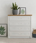 White dresser with four drawers and brushed nickel cabinet pulls, decorated with plants and wall art, modern bedroom decor