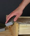 Hand using Pro Grade Sanding Sponges Pack Three By Five By One Inch Medium And Fine Grit For Contours And Flat Surfaces DIY Friendly Flexible Rinse And Reuse Aluminum Oxide Abrasive All Four Sides Ideal For Drywall Joint Finishing 2 Pack on wooden surface