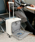 Person sitting beside 16 Inch Underseat Carry On Luggage Hard Shell With Spinner Wheels Airline Approved TSA Lock Front Pocket Ultra Lightweight Personal Item For Women And Men White in airport lounge.