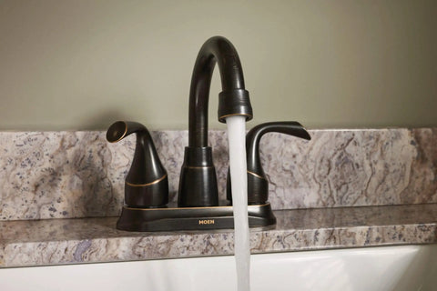 Idora Mediterranean Bronze Two Handle Centerset Bathroom Faucet With Drain Assembly High Arc Spout Easy Install 4 Inch Centerset Design Old World Style for sinks. Faucet with running water on marble countertop.