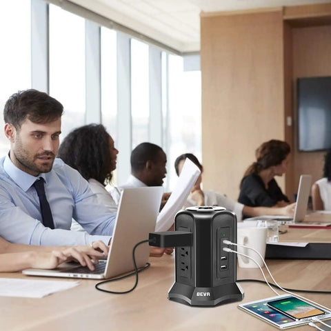 Power Strip Tower Surge Protector With Nine AC Outlets And Four USB Ports 900 Joules on office desk with people working.