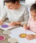 Mother and daughter using DIY Mandala Wind Chimes Craft Kit for Kids to color wooden ornaments on a table.
