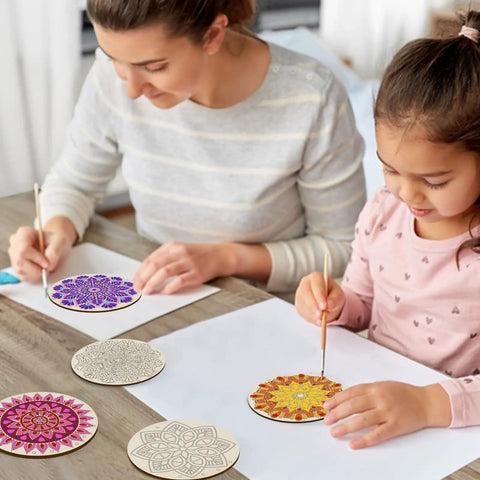 Mother and daughter using DIY Mandala Wind Chimes Craft Kit for Kids to color wooden ornaments on a table.