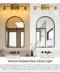 Vertical-striped glass vanity light shown turned on and off above an arched mirror with brushed gold fixtures.
