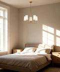 Muted Gold Chandelier With White Fabric Shades For Modern Farmhouse Linear Island Lighting In Kitchen And Dining Room, 5-Light Fixture, 60 Inch Chain, Cozy Warm Glow Vibe over bed in sunlit bedroom.