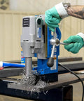Front view of Hougen HMD900 magnetic drill, blue and gray with T-handle, mounted on a metal table with metal shavings.