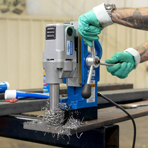 Front view of Hougen HMD900 magnetic drill, blue and gray with T-handle, mounted on a metal table with metal shavings.