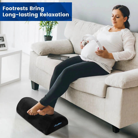 Pregnant woman using under desk foot rest with soft foam and washable removable cover for home office and car use on a couch.