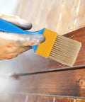 Hand using 2 Inch Nylon Bristle Paint Brush with Plastic Handle on wooden surface for DIY home projects, indoor and outdoor use.