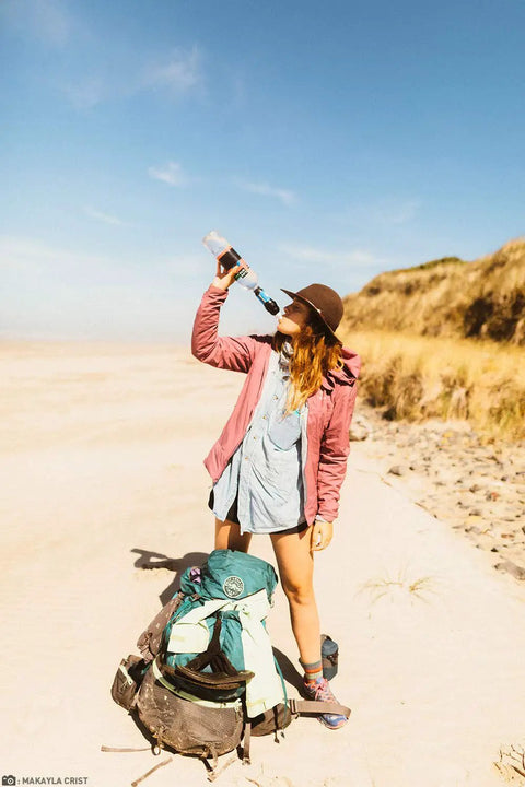 Person drinking from Portable Squeeze Water Filtration System With Two 32 Oz Pouches, Straw, And Hydration Pack Adapter on beach