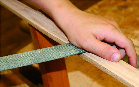 Heavy Duty Three Piece Wood Rasp File Set With Eight Inch Round Half Round And Flat Steel Files Featuring Soft Rubber Grip Handles For Pro Carpenters Knocking Down Rough Surfaces And Smoothing Hardwood Like A Champ, hand using file on wood surface.
