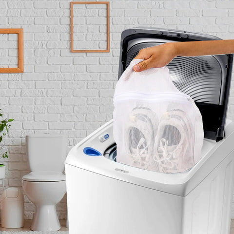 Hand placing sneakers in washing machine using Durable Sneaker Laundry Bag With Zipper And Straps, Honeycomb Mesh Wash And Dry Net