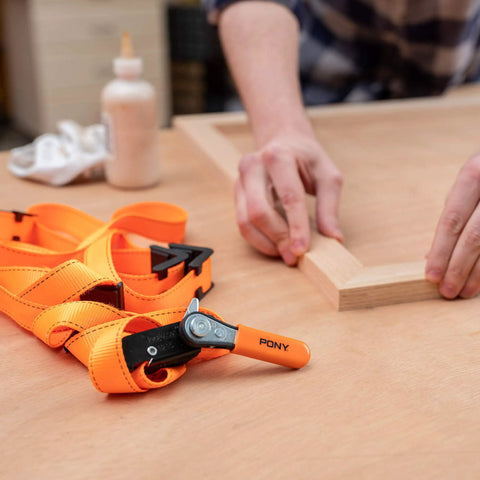 Heavy-Duty Adjustable Band Clamp For Woodworking And Framing, 15-Foot Strap, Self-Locking Ratcheting Handle on woodwork table.
