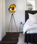 Lit Modern Tripod Floor Lamp In Black Finish With Gold Foil Circular Shade And Leather Accented Legs in bedroom corner