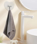 Heavy Duty Adhesive Wall Hooks With Slick Grip Keep Your Towels And Gear Locked In Place Zero Drilling Hassle Clear Transparent Look Fits Any Room Flawlessly, holding a gray towel in a bathroom setting.