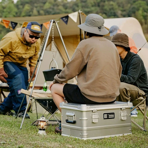 Rugged Folding Storage Box With Lid Heavy Duty Aluminum Frame Stackable Gear Crate Built Tough For Camping And Picnics No Sweat Organization Haul Your Stash On The Go Rust Resistant Silver Design used as a seat and storage at a campground.