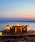 Waterfront deck with table adorned with 24 Pack Battery Operated Tea Lights Candles With Realistic LED Flicker, creating a serene atmosphere.