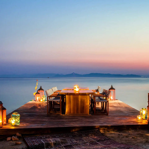 Waterfront deck with table adorned with 24 Pack Battery Operated Tea Lights Candles With Realistic LED Flicker, creating a serene atmosphere.
