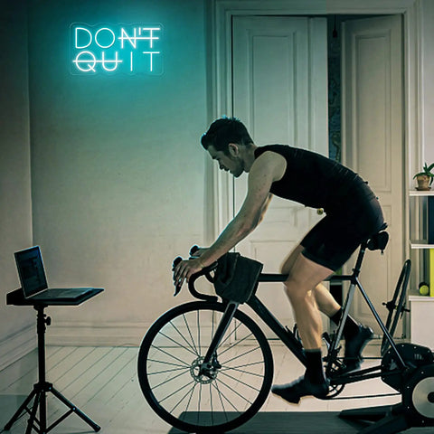Man cycling indoors with DO IT LED Neon Sign For Wall Decor USB Powered Switch Neon Lights For Office Gym Man Cave And Gaming Room Vibe Motivational Wall Art glowing behind