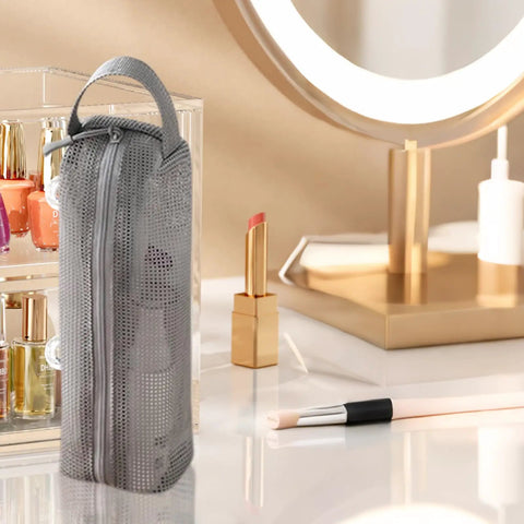 Gray travel toiletry bag with ventilated mesh storage on vanity table near makeup, road trip ready kit.