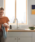 Precept Pull-Down Kitchen Faucet, 1.5 GPM Flow, Stainless Finish in modern kitchen with woman drying dish
