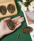 Four Pack Antique Oval Drawer Pulls in Antique Bronze, Vintage Floral Engraved Handles for Furniture, displayed with hand for scale