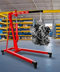 Heavy Duty 2 Ton Folding Hydraulic Engine Hoist Handling Up To 4000 Pounds Without Breaking A Sweat For Home Garages And Pro Auto Shops lifting an engine in a warehouse.