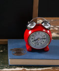 Two Piece Steel Clock Mainsprings Replacement Kit next to red alarm clock on blue book