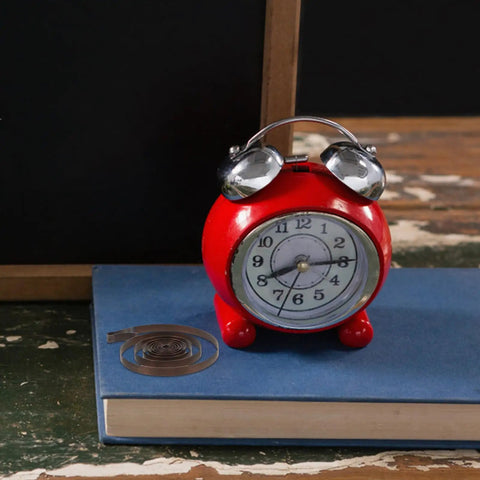 Two Piece Steel Clock Mainsprings Replacement Kit next to red alarm clock on blue book