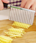 Stainless steel crinkle cutter with black handle slicing crinkle-cut potatoes on a wooden cutting board