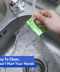 Green-handled stainless steel onion slicer with comb blades, being rinsed under running water in a sink.
