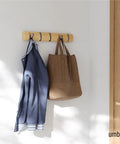 Flip 5 Wall Mounted Hook With Retractable Hooks for coats and bags in natural wood, mounted on white wall by door