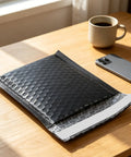 100 Pack 5 By 6 Inch Black Poly Bubble Mailers self seal padded envelope on a wooden table near a phone and coffee cup