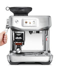 Certified Remanufactured Automatic Espresso Machine With Built In Grinder And Steam Wand showing user hand gripping portafilter.
