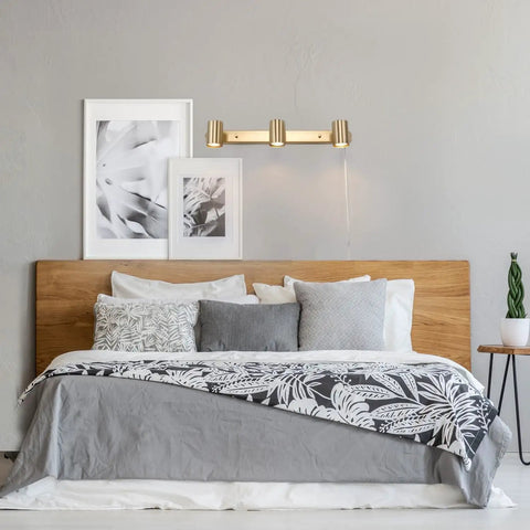 Three Light Plug-In Track Lighting in Matte Brass with Adjustable Heads above bed, wall-mounted, 15-foot cord visible