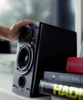 Hand adjusting R1850DB Dope Active Bookshelf Speakers With Bluetooth And Optical Input Built In Amplifier next to books