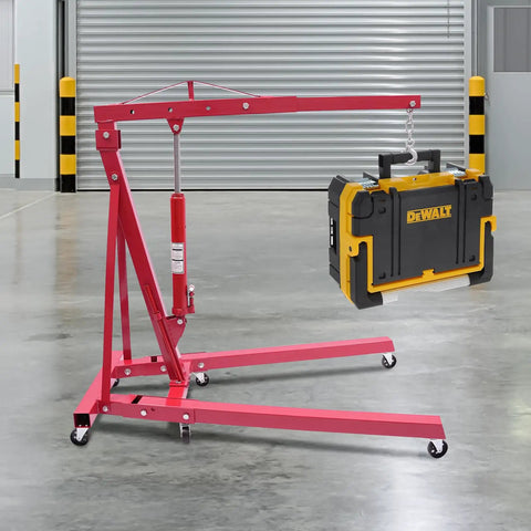 Premium Heavy Duty 1 Ton Folding Hydraulic Engine Hoist Shop Crane With Wheels lifting a DEWALT tool case in a garage.