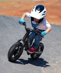Child riding Kids Electric Balance Bike BK1 With 12 Inch Tires, 150W Peak Motor, on a slope, wearing helmet and gloves