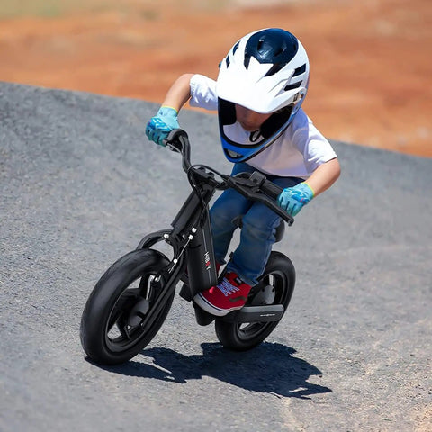 Child riding Kids Electric Balance Bike BK1 With 12 Inch Tires, 150W Peak Motor, on a slope, wearing helmet and gloves