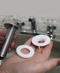 Hands holding chrome kitchen sink hole cover that hides unused holes from sprayer or soap dispenser, parts view