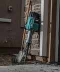Badass Heavy Duty Eighty Volt Brushless Cordless Breaker Hammer with shovel leaning against a stone wall.
