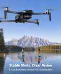 Pocket Size Drone With 4K UHD Camera And 3 Axis Gimbal flying over lake with paddleboarders, mountains in background.