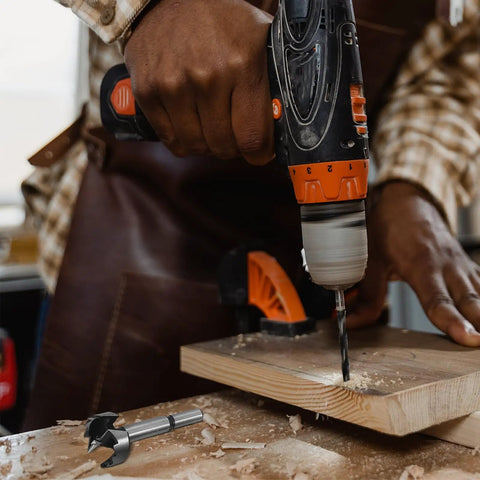 User holding a drill with a Forstner bit, working on wood, showcasing Top Shelf 5 Piece Forstner Drill Bit Set Woodworking Hinge Cutter Round Shank Multi Tooth Bits For Hardwood Softwood Plywood Delivers Knockout Precision And Solid Wooden Carrying Case.