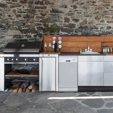 Outdoor kitchen with stainless steel barbecue grill, cabinets, and dishwasher against stone wall backdrop