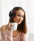 Woman wearing Kick Loud Noise To The Curb With Double Layer Over Ear Earmuffs, holding a cup while working at a laptop.