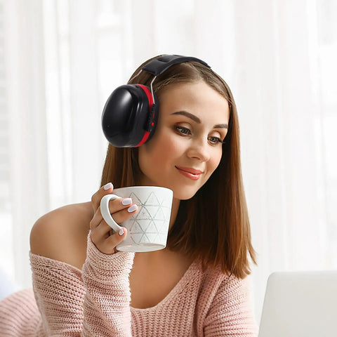 Woman wearing Kick Loud Noise To The Curb With Double Layer Over Ear Earmuffs, holding a cup while working at a laptop.