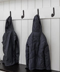 Four Pack Badass Cast Iron Wall Hooks In Rustic Black Vintage Coat Rack Heavy Duty Entryway Storage Organizer With Pre Drilled Screws For Jackets Bags And Everyday Gear holding two jackets on a white wall.