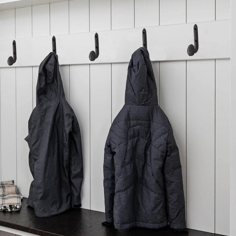 Four Pack Badass Cast Iron Wall Hooks In Rustic Black Vintage Coat Rack Heavy Duty Entryway Storage Organizer With Pre Drilled Screws For Jackets Bags And Everyday Gear holding two jackets on a white wall.
